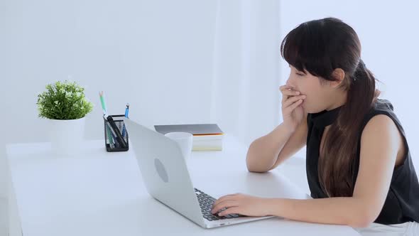 Young freelance asian woman working on laptop computer drinking coffee when sleepy. alt