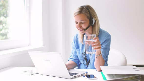 Businesswoman sitting at desk using headset and laptop alt