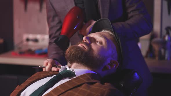 Stylish Man Sits in a Barbershop While a Barber Dries His Beard