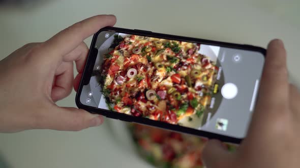 Woman takes picture of cooked pizza on plate at table