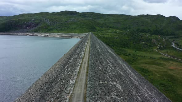 Drone view of Norwegian Dam overlooking lush green fields and mountains. Aerial flying across top of alt