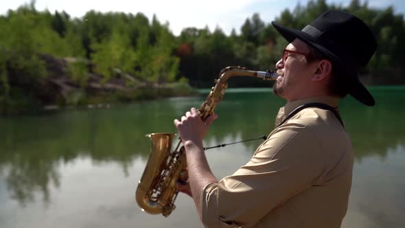 Jazz Musician Is Playing Saxophone on Shore of Lake in Forest, Medium Portrait alt
