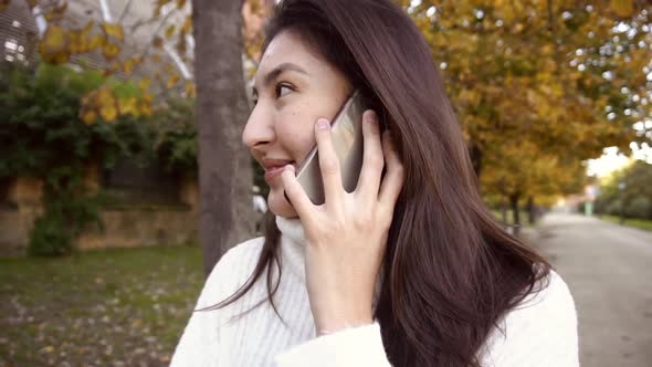 Slow Motion Asian Happy Girl Wearing White Sweater Talking By Smartphone and Walking in Park.