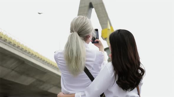 Asian lesbian couple enjoying travel in Thailand and using a smartphone taking photo.