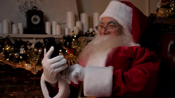 Modern Smiling Santa Claus Works on Smartphone Buys Christmas Gifts on Internet alt