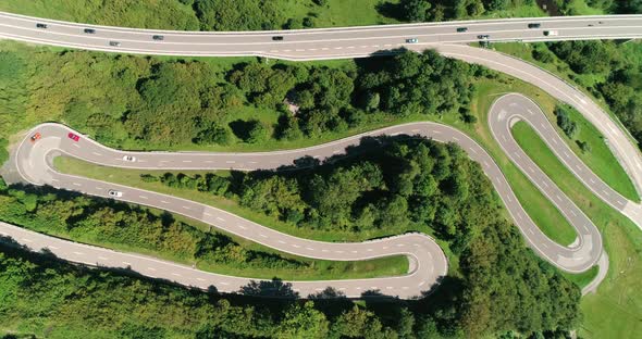 Aerial View Top Down of Racing Cars Ferrari and Jaguar Driving a Serpentine Mountain Road in Swiss alt