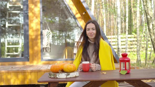 Happy Young Woman Drinking Coffee Sitting at the Wooden Table Outdoors