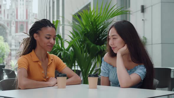 Asian Girl and African American Female with Dreadlocks Cute Talking and Drinking Coffee Outdoors alt