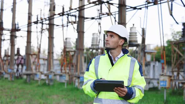 Male Engineer in Uniform and Helmet Standing Outdoor and Tapping on Tablet alt
