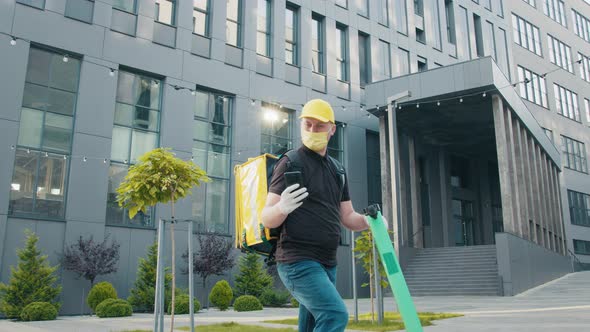Food Supplier with Termo Backpack Riding on Electric Scooter on the Street alt