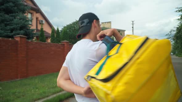 Live Camera Follows Yellow Delivery Bag As Young Man Putting on Backpack Walking alt