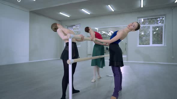 Three Flexible Slim Elegant Women Rehearsing Ballet Dance at Barre Bending Back Raising Hand alt