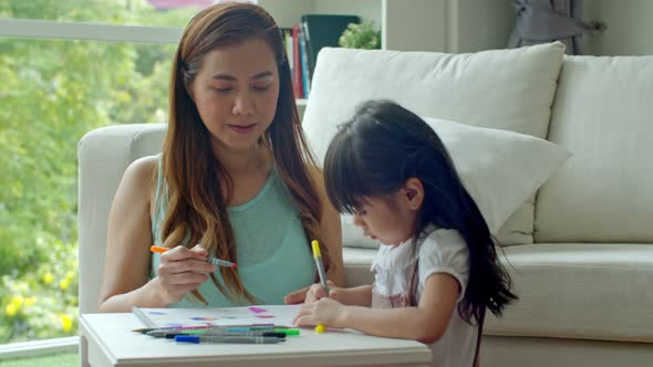 Cheerful young mother and daughter drawing on paper