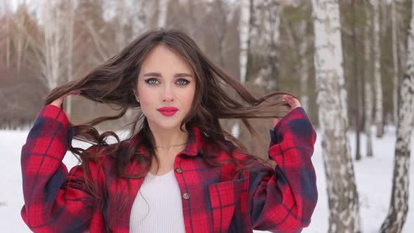 Young Woman with Wavy Hair Standing and Touching Face in Winter Forest