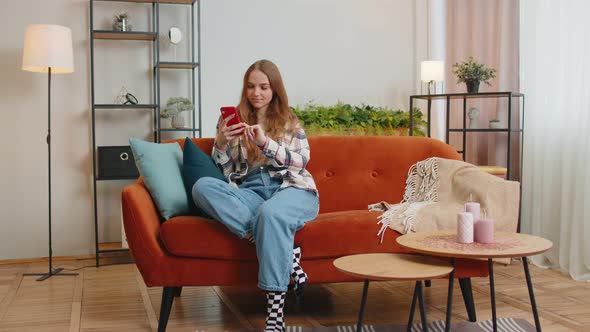 Cheerful Young Woman Sitting on Sofa Using Mobile Phone Share Messages on Social Media Application alt