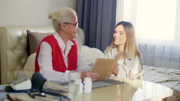 Senior Woman Reading a Book and Speaking with Granddaughter at Home