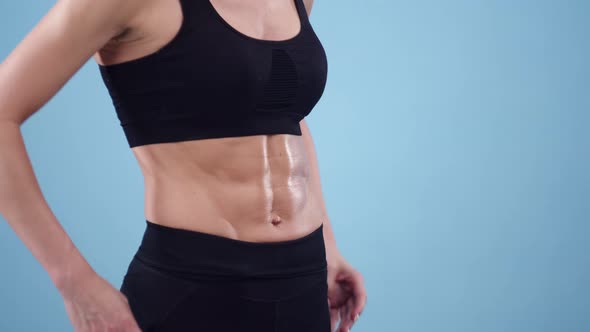 Athletic woman with abs puts her hands on her waist and draws in stomach on blue background alt