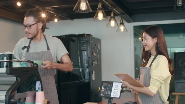 Asia female and male barista waiter taking order from customer standing together behind bar counter. alt