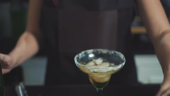 Close up of bartender pouring tequila into margarita glass with a lime. alt