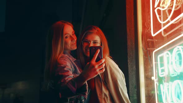 Two Millennial Women Pose on Phone Camera in Neon alt