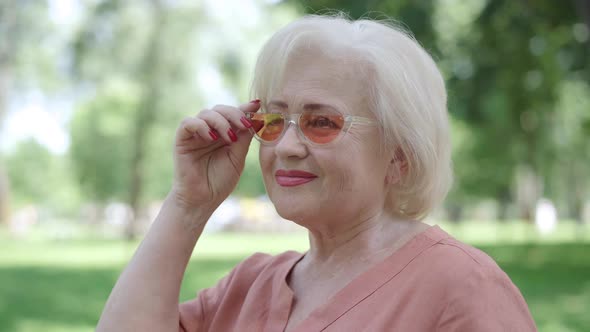 Carefree Senior Woman Turning To Camera, Putting Down Sunglasses, Winking and Smiling. Portrait of alt