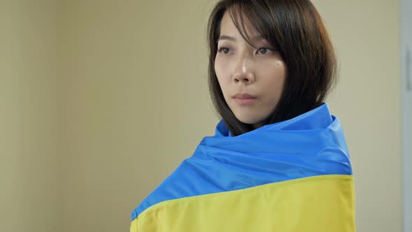 Portrait of an Asian Woman with a Ukrainian Flag on Her Shoulders alt
