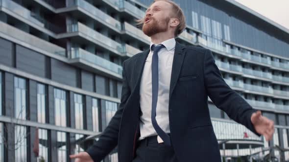 Positive Euphoric Young Businessman with Beard Dancing in Front the Office Center Mirrored Building