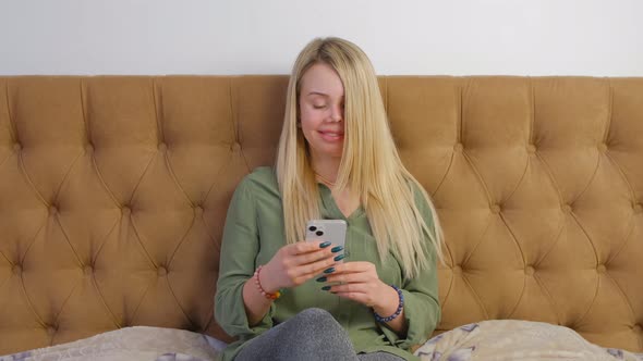 Woman browsing social media news feed and internet on new smart phone in bedroom alt