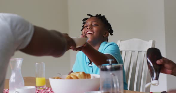 African american boy smiling while having breakfast together with his family at home alt