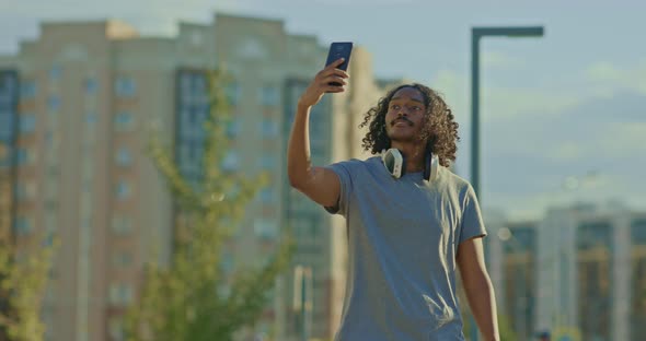 Young Man Walks and Takes Pictures on a Mobile Phone a Selfie for Friends