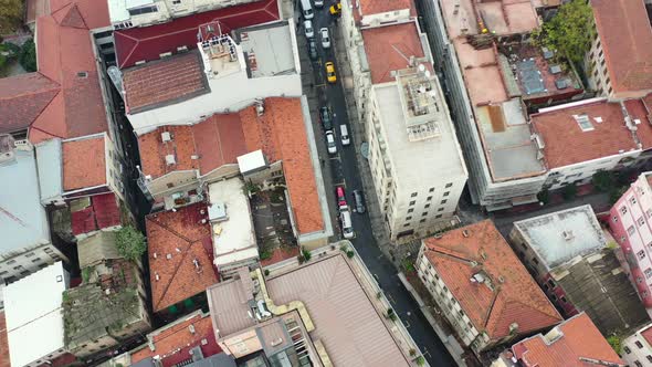 Aerial top down view of cars driving down a narrow alley street surrounded by tall European resident alt
