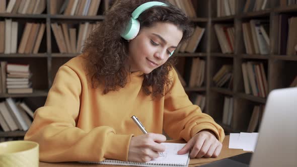 Hispanic Teen Girl Student Wear Headphones Watching Webinar Class Making Notes alt