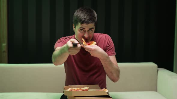 Portrait of Young Man Watching TV Eating Pizza Sitting on Sofa at Home