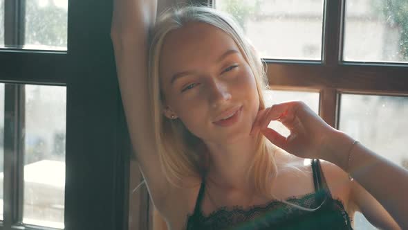fashion portrait of a beautiful young woman with blue eyes and blonde hair poses near the window alt