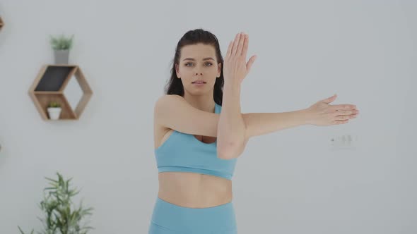 Active woman in blue sportswear  stretching arms and body doing exercises at home looking at camera alt