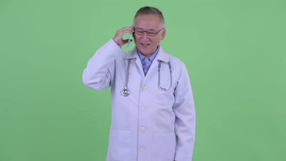 Happy Mature Japanese Man Doctor Talking on the Phone While Using Digital Tablet alt