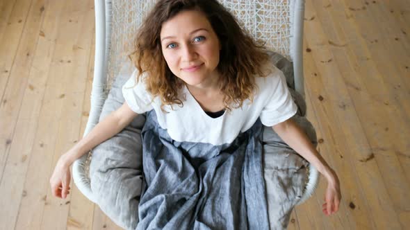 Young European Girl in a Linen Dress Swings in a Hammock-swing in a Loft Apartment and Looks Up alt