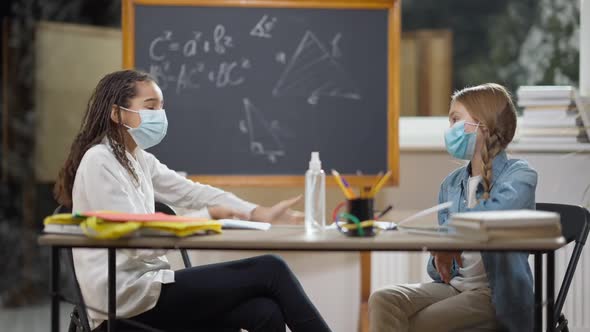 Junior High Students in Covid19 Face Masks Sitting at Desk in Classroom Talking alt
