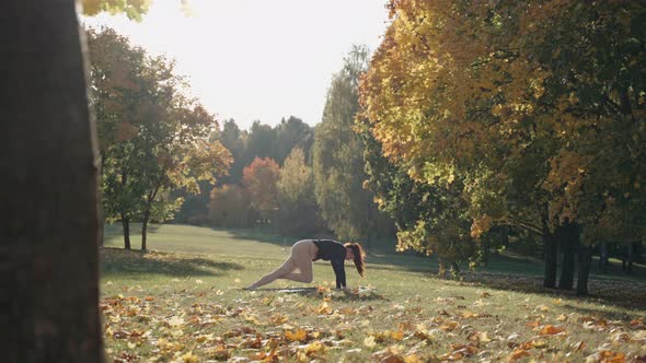 Young Woman Doing Side Plank on One Leg in Autumn City Park on a Yoga Mat