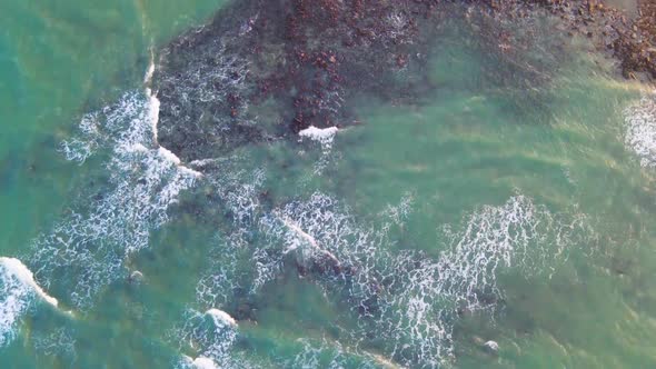 Calm waves from turquoise ocean hits rocky surface. Aerial seascape clip. alt