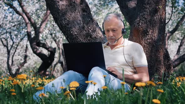 An Elderly Grayhaired Businessman Man with Headphones Indignant and Swearing on the Online