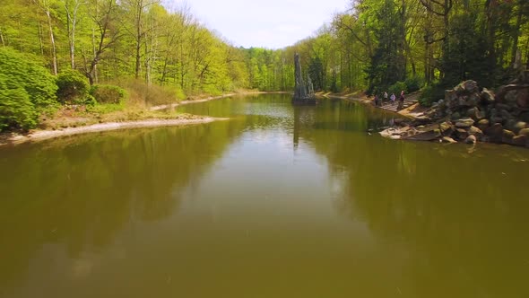 Drone fast footage of a lake in a forest park,  a beautifully designed concrete, curb foot bridge co alt