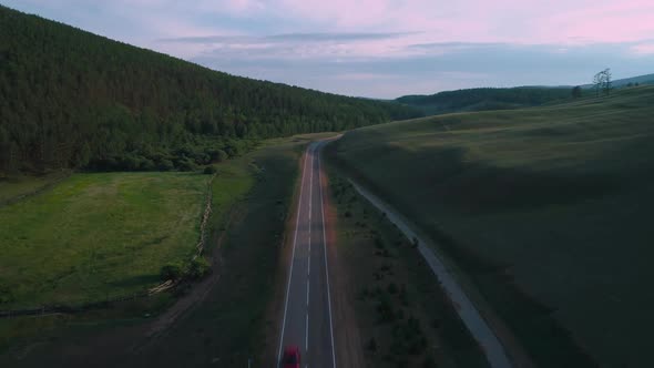 AERIAL, TOP DOWN: Dark Colored Car Driving Down an Asphalt Road Crossing the Vast Forest on a Sunny alt