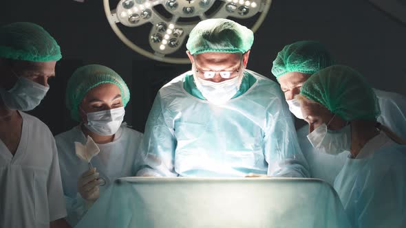 Friendly Team of Confident Concentrated Caucasian Surgeons in Operating Room with Surgery Equipment alt