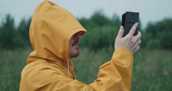 Man in Yellow Raincoat with Hood is Trying to Catch GPS or Internet in Nature alt