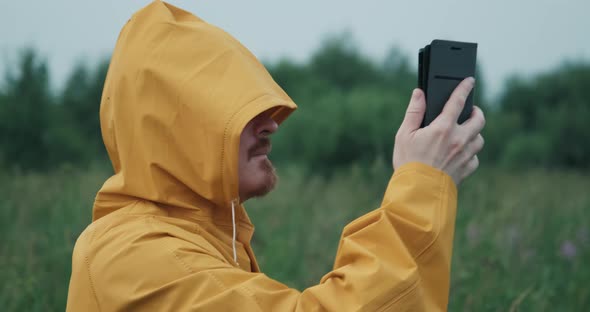 Man in Yellow Raincoat with Hood is Trying to Catch GPS or Internet in Nature