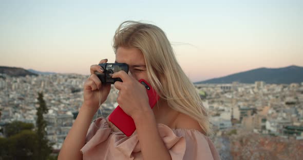 a Woman at the Top of the Mountain Takes a Picture of the City on an Old Camera alt