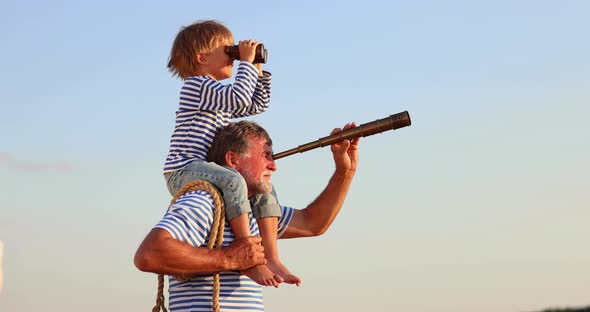 Grandfather and boy with telescope having fun outddor against blue summer sky