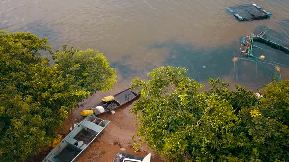 Drone view of boats and fishing equipment sitting on the shore of a lake on a fishing farm in the To alt
