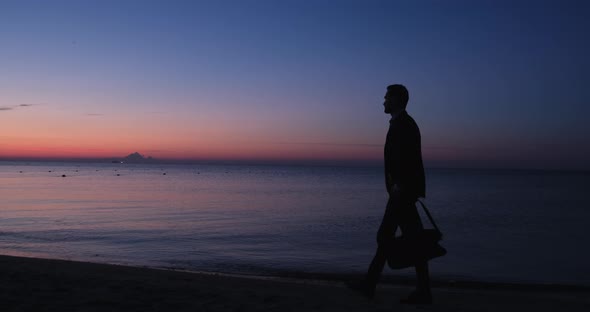 Silhouette of a man with a bag at dawn by the sea.